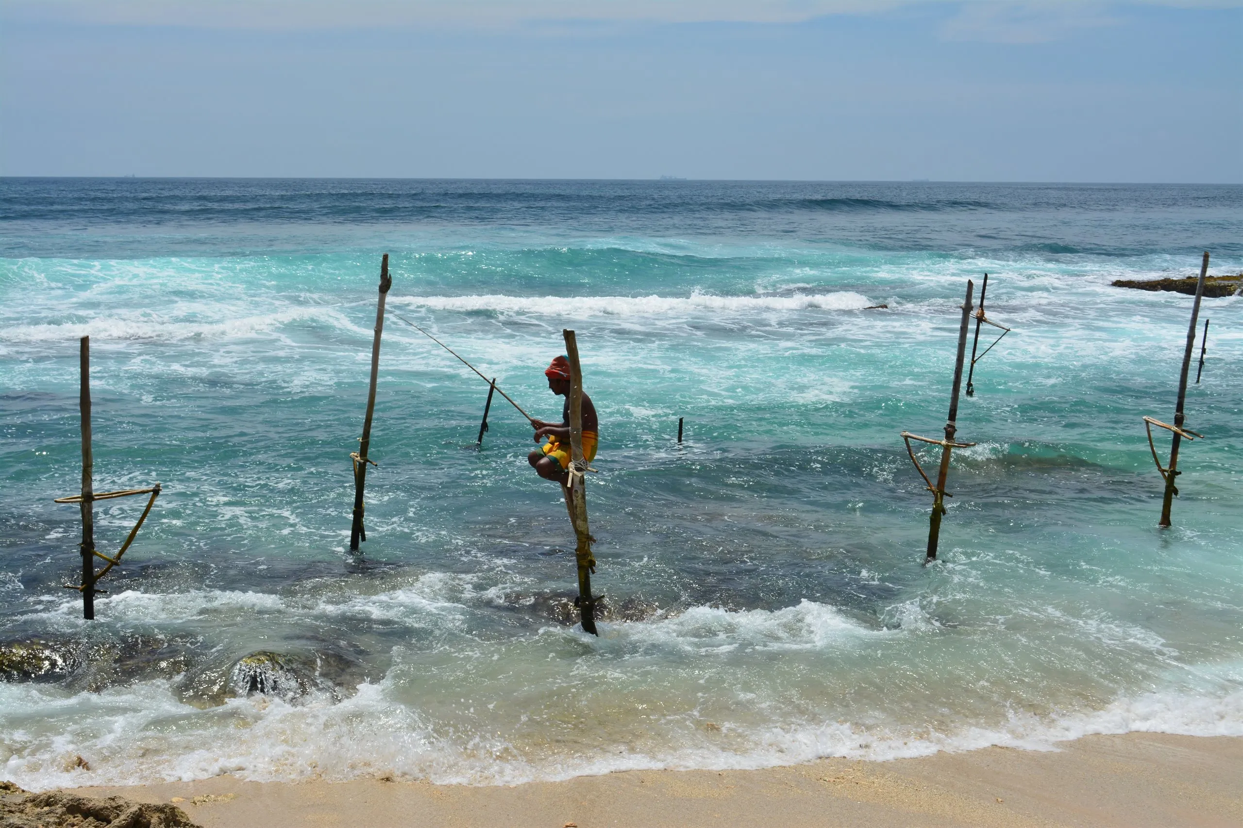 A stilt fisherman sitting on his pole in the shallows