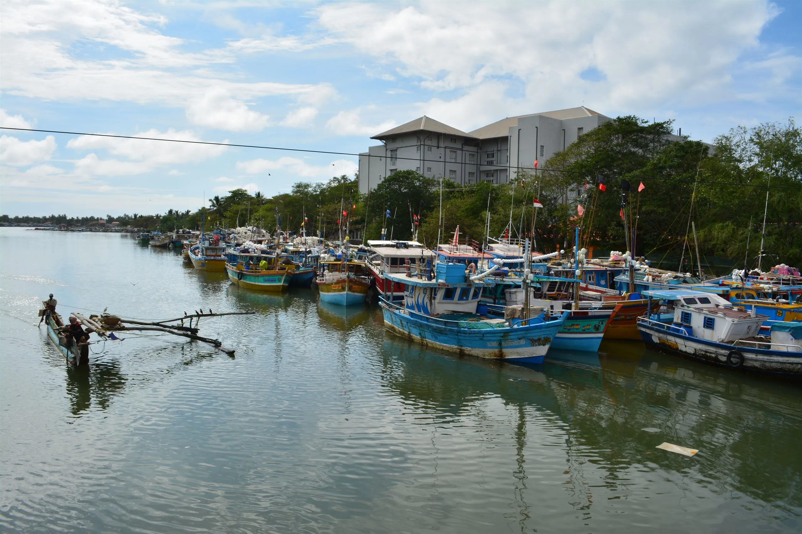 Fishing boats moored in the lagoon at Negombo, an outrigger canoe heading out