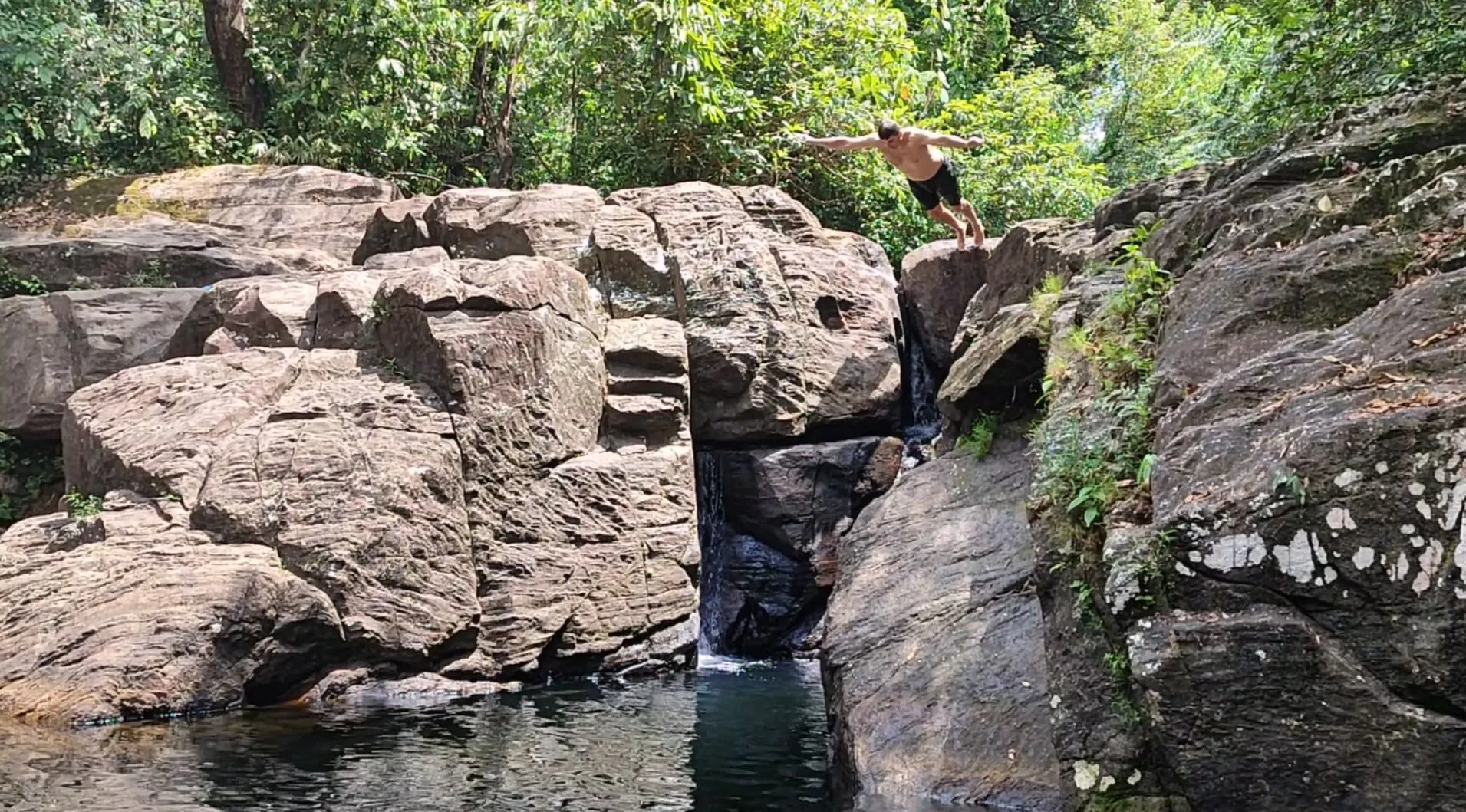 A guest mid-jump from a rock into the pool below a waterfall