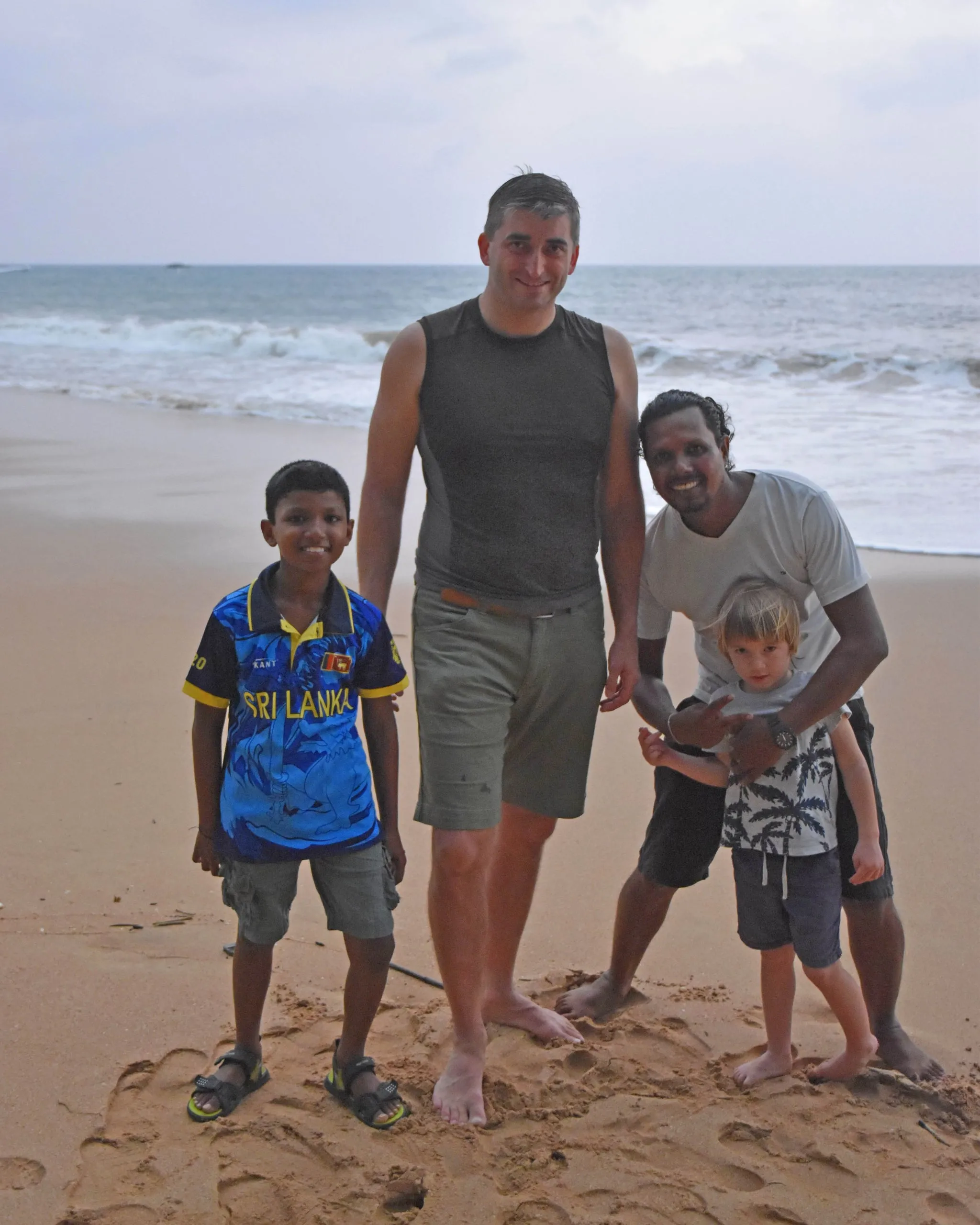 A tall visitor and a guide standing on the beach at dusk with two boys, one Sri Lankan and one Czech